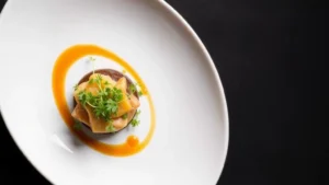 Overhead shot of artfully plated fine dining dish with microgreens, sauce swoosh, and polished white plate against dark background, professional restaurant photography