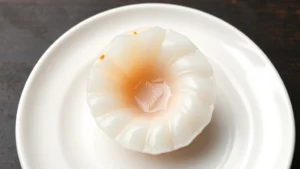 Overhead shot of pristine raw hokkaido scallop (hotate) on white ceramic plate, delicate translucent flesh with subtle golden undertones, minimalist plating, professional sushi photography