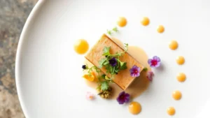Overhead shot of an elegantly plated first course featuring delicate protein with microgreens, edible flowers, and artistic sauce dots on white porcelain plate, professional restaurant photography