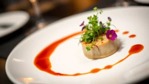 Artfully plated fine dining dish with microgreens, edible flowers, and artistic sauce application on white ceramic plate, professional restaurant lighting, shallow depth of field, food photography studio style