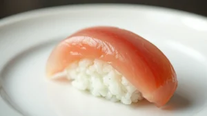 Close-up of pristine nigiri sushi with translucent fatty tuna and perfectly formed rice mound, glossy surface reflecting light, minimalist white ceramic plate, professional culinary photography