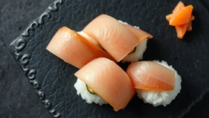 Close-up overhead view of artfully arranged nigiri sushi pieces on a dark slate plate, showcasing translucent fish slices draped over perfectly shaped rice mounds, with delicate garnish and ginger slices visible, professional culinary photography, natural soft lighting highlighting the fish's texture and sheen